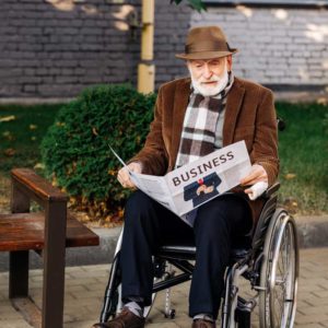 an elderly man in a wheelchair reading a paper