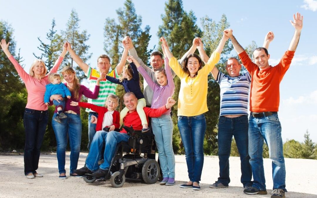 group of people standing around a man in a wheel chair, holding hands above their head in victory