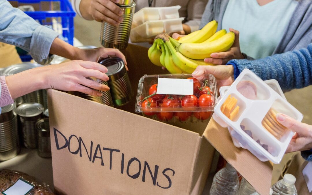people gathered around a box marked "donations" with food and cans to donate