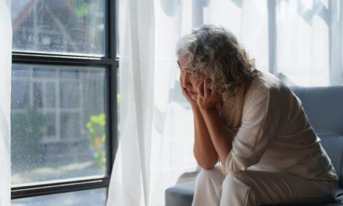 an elderly woman staring out a window forlornly